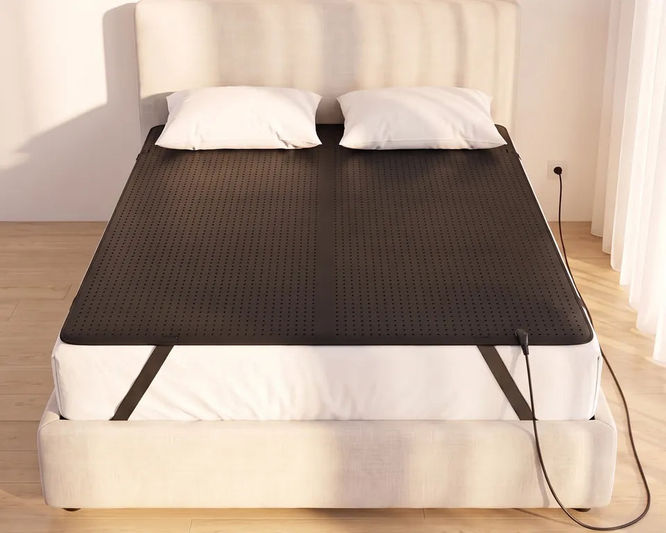 La alfombrilla GroundingFlow cubriendo todo el colchón de borde a borde con sus correas de esquina puestas, y el cable conectado al enchufe de la pared
