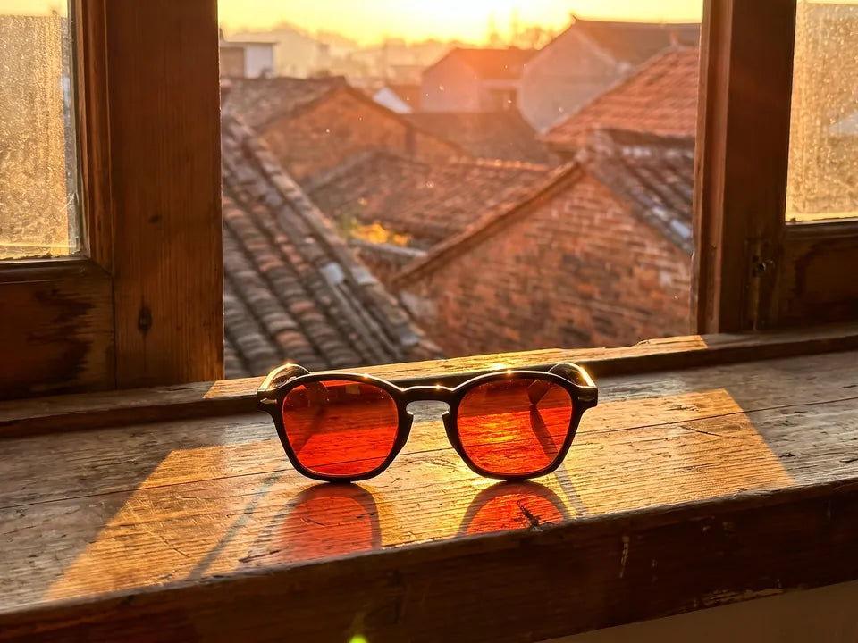 Óculos de lentes vermelhas no parapeito de uma janela ao pôr do sol